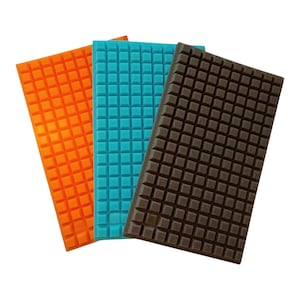 May include: Three rectangular foam pads in orange, teal, and brown. Each pad has a grid pattern of small, raised squares across its surface. The pads are arranged at slightly different angles, showcasing their textured design.