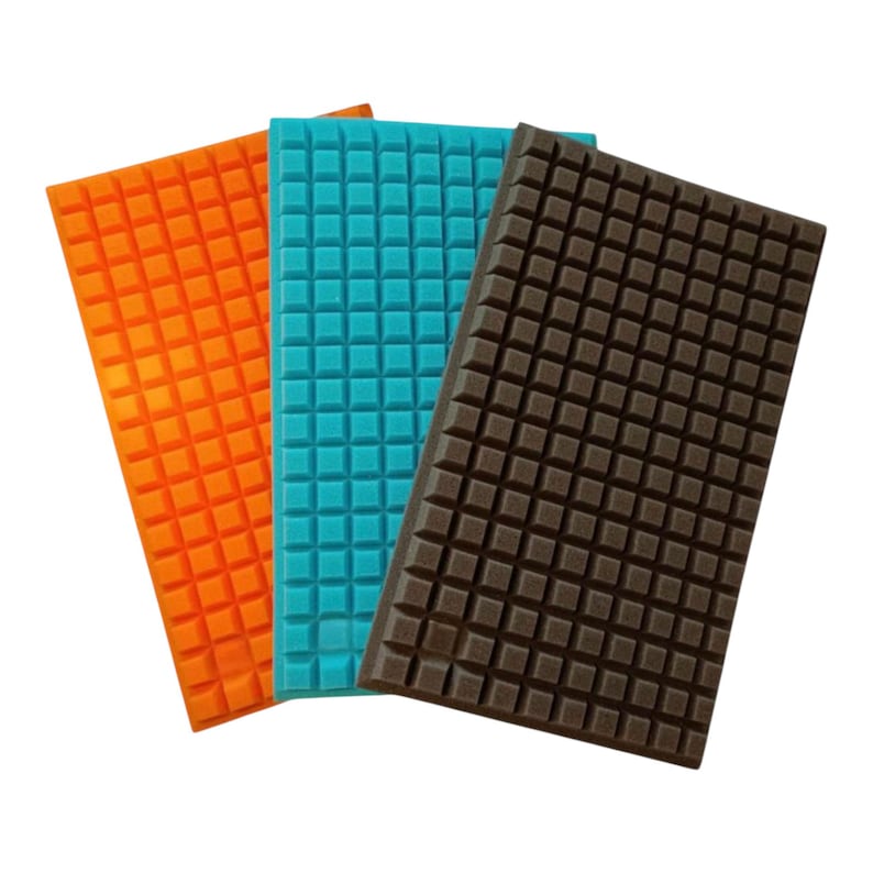May include: Three rectangular foam pads in orange, teal, and brown. Each pad has a grid pattern of small, raised squares across its surface. The pads are arranged at slightly different angles, showcasing their textured design.
