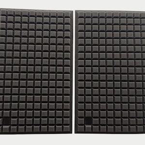 May include: Two rectangular black acoustic foam panels with a grid-like pattern of small, square protrusions. The panels are side by side against a white background, designed for sound absorption in a studio or home theater.