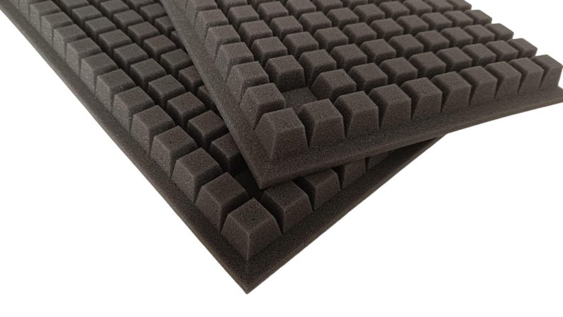 May include: Two dark gray foam sheets with a grid of square protrusions. The foam has a textured surface and is designed to absorb sound. The sheets are rectangular and are likely used for soundproofing or acoustic treatment.