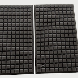 May include: Two black speaker covers with a square grid pattern. Each cover has a small JBL logo in the lower corner. The covers are rectangular and appear to be made of a foam-like material.