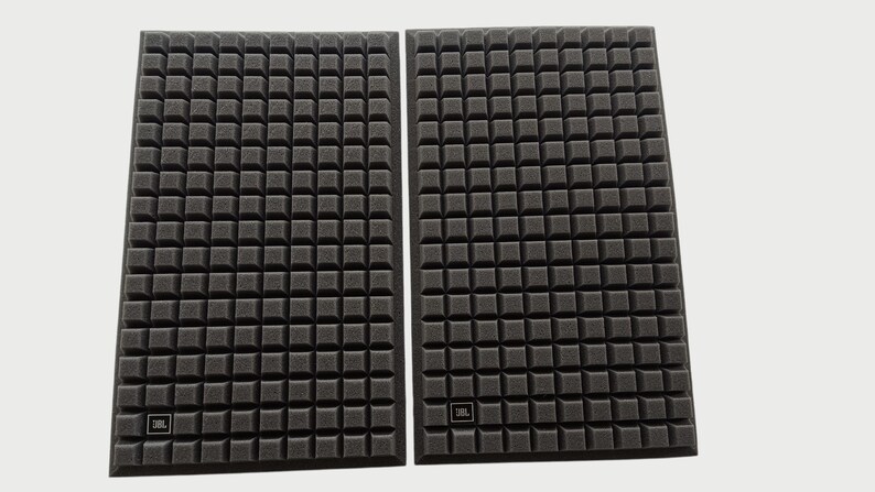 May include: Two black speaker covers with a square grid pattern. Each cover has a small JBL logo in the lower corner. The covers are rectangular and appear to be made of a foam-like material.
