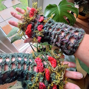 May include: Crochet fingerless gloves in green, purple, and yellow, with red detailing. The openwork design provides flexibility. These handmade gloves are a unique accessory. The gloves are a statement piece, adding a touch of artistry to any outfit.