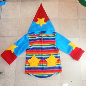 May include: A colourful striped fleece jacket with a blue hood and red sleeves. The jacket has a zip closure and features yellow star appliques on the hood and sleeves.