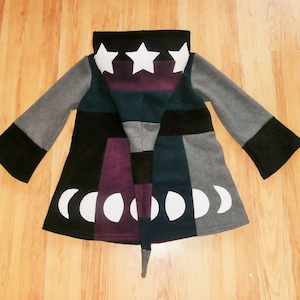 Könnte beinhalten: Eine graue, schwarze, blaugrüne und violette Kapuzenjacke mit Patchwork-Design. Die Kapuze hat weiße Sterne darauf und der Saum der Jacke hat weiße Halbmonde.