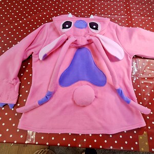 Puede incluir: Mono con capucha rosa con un dise&ntilde;o de personaje, con orejas grandes, una nariz morada y una cola. El mono tiene una capucha con ojos y antenas de personaje. Las mangas terminan en detalles de garras. Un atuendo divertido y tem&aacute;tico.