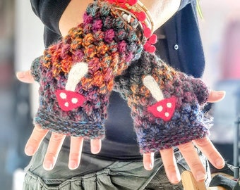 May include: A pair of colorful crocheted fingerless gloves with mushroom appliques. The gloves are made with a variety of colors, including red, orange, yellow, green, blue, and purple. The mushrooms are white with red tops and white spots.