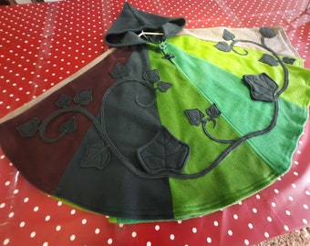 May include: A hooded cape in shades of green, brown, and gray, with a leaf design. The cape is made of soft fabric and features a pointed hood. The leaf design is a darker shade of gray and is sewn onto the cape.