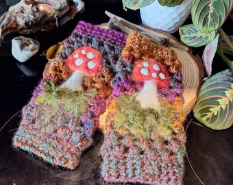 May include: A pair of colorful, crocheted fingerless gloves. Each glove features a red mushroom with white spots, set against a backdrop of green, purple, and orange yarn. The gloves are designed with a textured stitch.