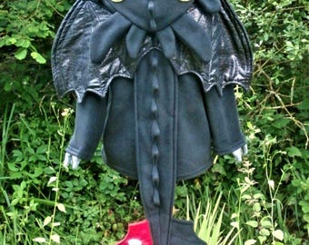 May include: A black dragon costume with yellow eyes, a crown, and a long tail. The costume has a red and white wing detail and is displayed on a yellow stand. The costume is made of soft fabric and is designed to resemble a dragon.