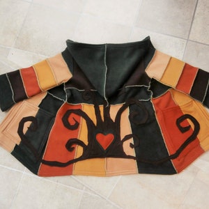 May include: A hooded fleece jacket with a patchwork design featuring stripes of brown, orange, and beige. The jacket has a large, embroidered heart with vines on the front.
