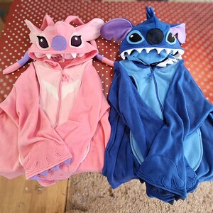 Puede incluir: Dos monos con capucha tem&aacute;ticos de personajes. Uno es rosa con un dise&ntilde;o blanco en el pecho y una cara de personaje en la capucha. El otro es azul con una cara de personaje en la capucha. Ambos tienen cremalleras y detalles de personajes.