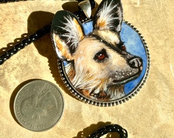 Peut inclure: Un collier pendentif avec une illustration détaillée d'un lycaon. Le pendentif rond a un cadre argenté et un fond bleu. Le collier a une chaîne noire. Une pièce de monnaie est à côté du pendentif pour la comparaison de taille.