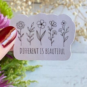 May include: White sticker with a black outline of five different flowers and the text "DIFFERENT IS BEAUTIFUL".