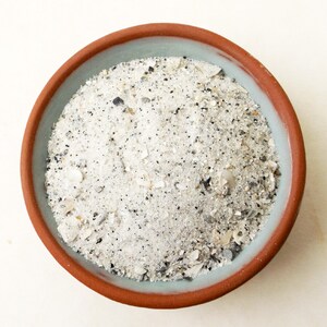 May include: A close-up of a terracotta bowl filled with white sand and small seashells.