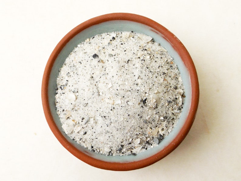 May include: A close-up of a terracotta bowl filled with white sand and small seashells.