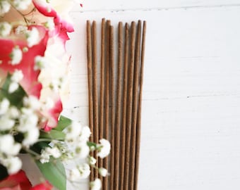 May include: A bundle of brown incense sticks on a white wooden surface. The sticks are arranged in a row and are about 10 inches long.