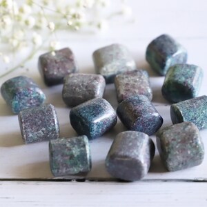 May include: A collection of tumbled blue and green kyanite stones with red and white inclusions. The stones are smooth and polished, and they have a variety of shapes and sizes.