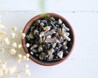 May include: A small bowl filled with a mixture of black, brown, and silver incense resins. The bowl is made of terracotta and has a dark green glaze.