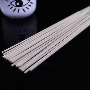 May include: A bundle of white incense sticks, arranged in a fan shape, on a black surface.