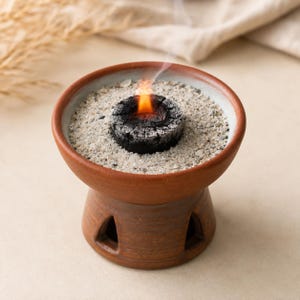 Sand in a charcoal burner with a lit charcoal on top.