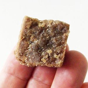 Fingers holding a square piece of amber resin incense on a white background.