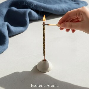 Incense stick being lit my a flame on a match on a neutral surface with a blue cloth in the background.