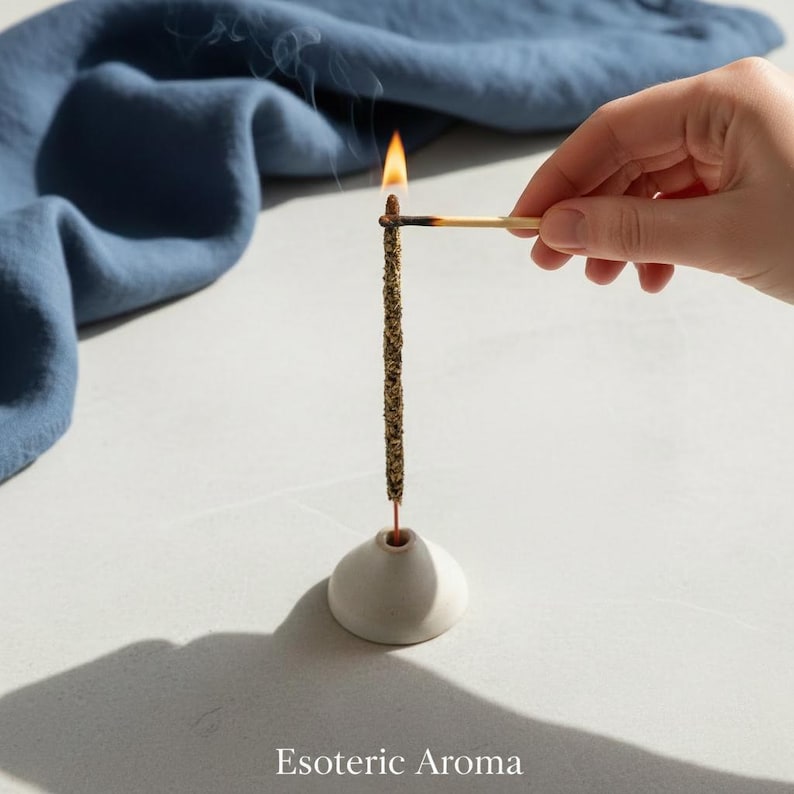Incense stick being lit my a flame on a match on a neutral surface with a blue cloth in the background.