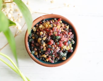 May include: A small terracotta bowl filled with colorful resin incense. The incense is a mix of red, green, yellow, and black pieces.