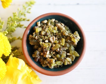 May include: A small terracotta bowl filled with green and gold resin crystals. The bowl is on a white surface.