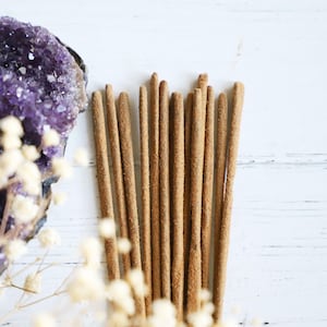 Incense sticks on a white background with an Amethyst crystal and white flowers nearby.