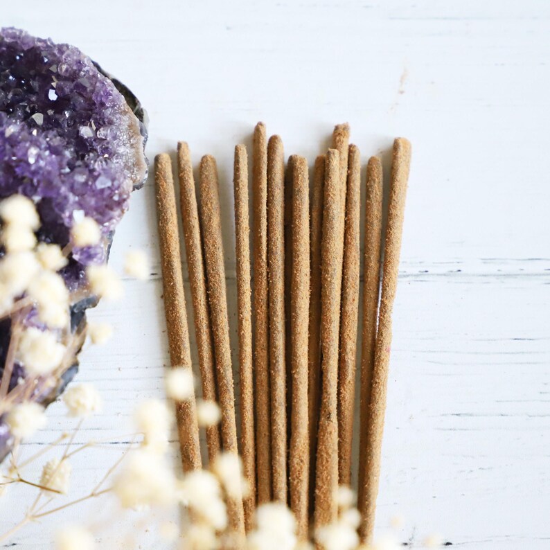 Incense sticks on a white background with an Amethyst crystal and white flowers nearby.