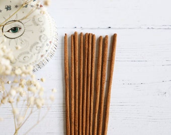May include: A bundle of brown incense sticks on a white wooden surface.