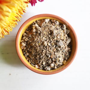 May include: A small orange bowl filled with a mixture of brown and tan resin pieces.