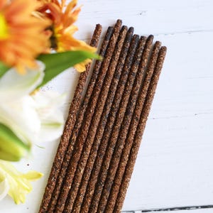 May include: A bundle of brown incense sticks arranged in a fan shape on a white surface. The sticks are about 10 inches long and have a rough texture.