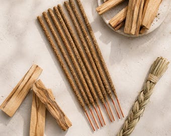 May include: A collection of eight brown incense sticks with orange bases, several light brown wooden palo santo sticks, and a braided bundle of dried sweetgrass. The text Esoteric Aroma is printed in small, dark letters at the bottom center.