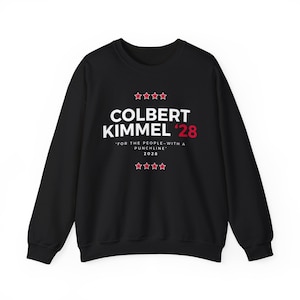 May include: Black crewneck sweatshirt with white text that reads "COLBERT KIMMEL '28" with red accents. Below the text is the phrase "FOR THE PEOPLE-WITH A PUNCHLINE" and the year 2028. Four red stars are above and below the main text.