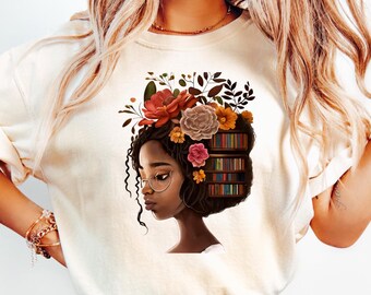 Può includere: T-shirt color crema con grafica del profilo di una donna con capelli decorati con fiori e libri. La donna ha la pelle scura e indossa occhiali. La maglietta è abbinata a jeans azzurri.