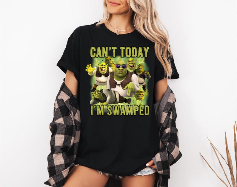 May include: Black t-shirt featuring a graphic of Shrek and other characters with the text "CAN'T TODAY I'M SWAMPED" in green and yellow. The image shows Shrek wearing sunglasses and other characters in various poses.