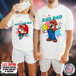 May include: White t-shirts with colorful graphic designs. One shirt says "RAD DAD" with a cartoon character holding a star. The other shirt says "RAD LIKE DAD" with a similar cartoon character. Both shirts have a retro 80s style.