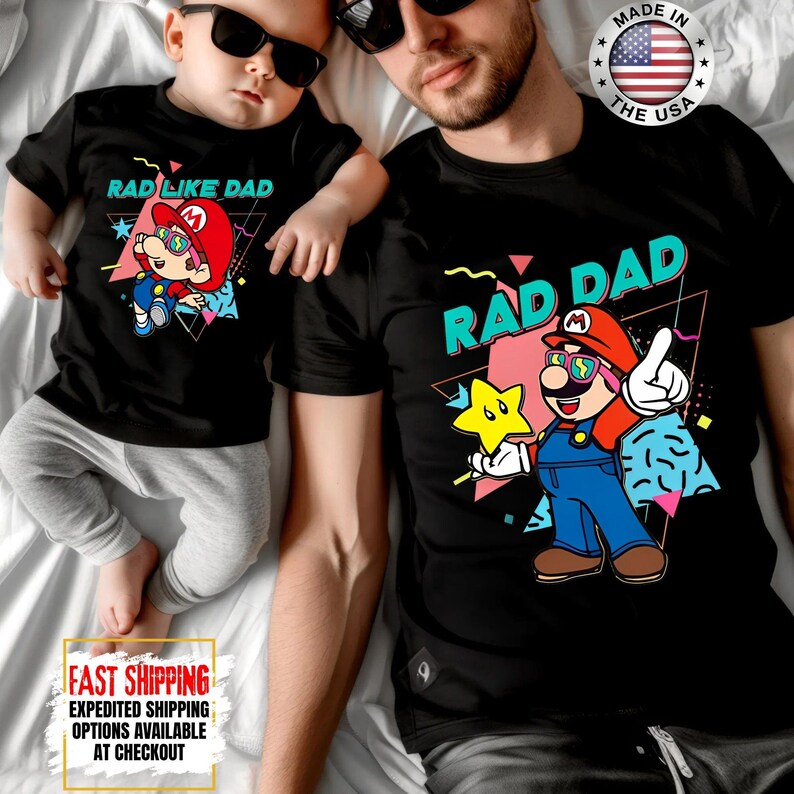 May include: Black t-shirts with matching graphics. One shirt says "RAD DAD" with a cartoon character holding a star. The other shirt says "RAD LIKE DAD" with a similar cartoon character. Both shirts have a retro design.