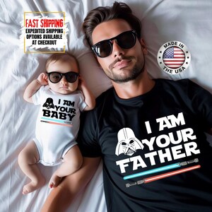 May include: A black t-shirt with the text "I AM YOUR FATHER" and a white Darth Vader graphic. A white baby onesie with the text "I AM YOUR BABY" and a Darth Vader graphic. Both shirts have lightsaber designs.