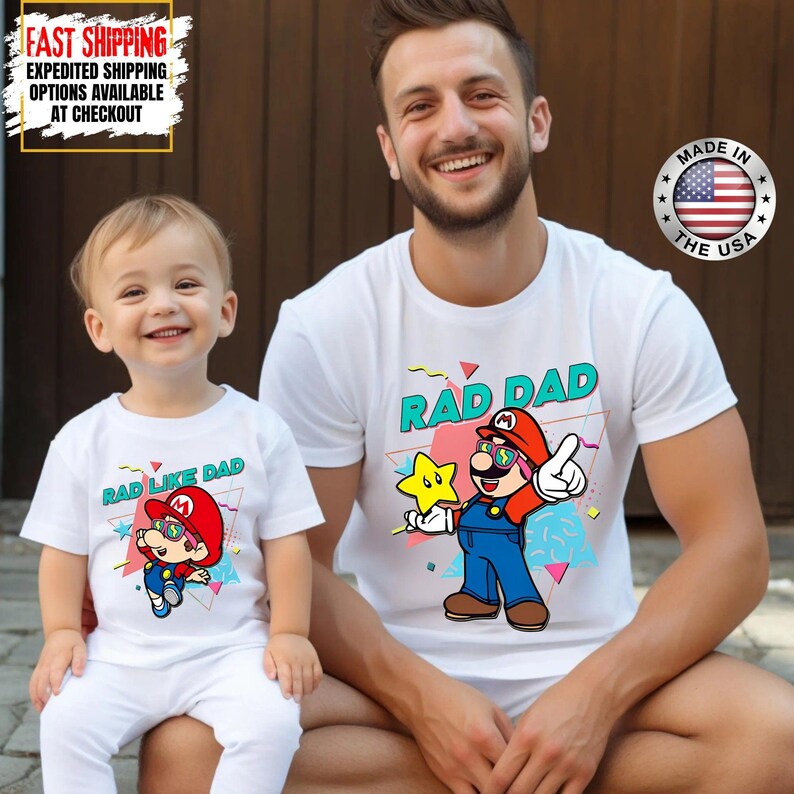 May include: White t-shirts with a cartoon graphic of a character wearing sunglasses and a red hat. The shirt on the right says "RAD DAD" and the shirt on the left says "RAD LIKE DAD". The shirts are made in the USA.