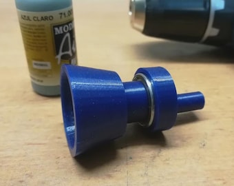 May include: A blue 3D-printed object with a bearing, next to a bottle of blue paint and a power drill. The object has a conical shape on one end and a cylindrical shape on the other.