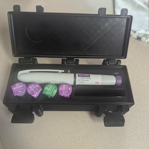 May include: A black plastic case containing a white and purple pre-filled pen and several purple and green BD Ultra Fine needle caps. The pen has text that reads "Once weekly 1 multiple-dose pre-filled pen 4 Doses".