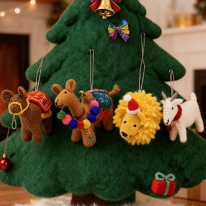 Könnte beinhalten: Ein grüner Weihnachtsbaum aus Filz, der mit Tierschmuck verziert ist. Zu den Ornamenten gehören ein Esel, ein Kamel, ein Löwe und eine Ziege. Der Baum ist außerdem mit einer Glocke, Schleifen und einem kleinen Geschenkornament geschmückt.