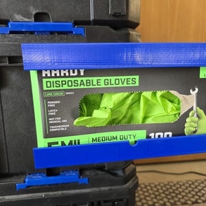 Może przedstawiać: Niebieska rama drukowana w 3D trzyma pudełko "HARDY DISPOSABLE GLOVES". Pudełko jest czarne z zielonym i białym tekstem i zawiera limonkowo-zielone rękawice. Rama jest zamontowana na czarnym pojemniku do przechowywania. Tekst na pudełku brzmi "MEDIUM DUTY."