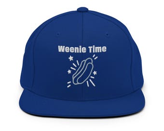 May include: A royal blue snapback hat with the phrase "Weenie Time" embroidered in white. A white outline of a hot dog with starbursts is below the text. The hat has a flat brim and a structured crown.