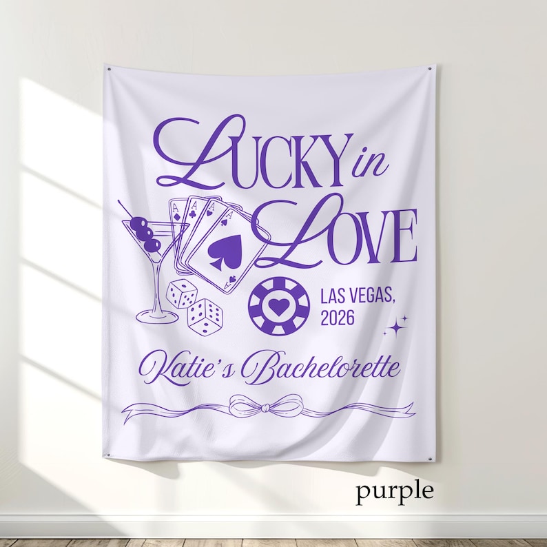 May include: White fabric banner with purple text and graphics. The banner reads "Lucky in Love" with Las Vegas, 2026, and "Katie's Bachelorette". Graphics include playing cards, dice, a martini, and a casino chip.