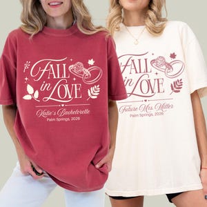 May include: Two short-sleeve t-shirts, one maroon and one cream, featuring the text Fall in Love with a ring graphic and leaf accents. The maroon shirt reads Katie's Bachelorette Palm Springs, 2026, while the cream shirt reads Future Mrs. Miller Palm Springs, 2026.